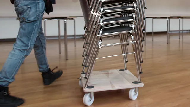 Ehrenamtlicher rollt Stapel mit Stühlen; Foto: Emmaus